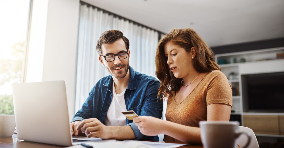 couple using laptop to make online purchase while holding credit card in hand