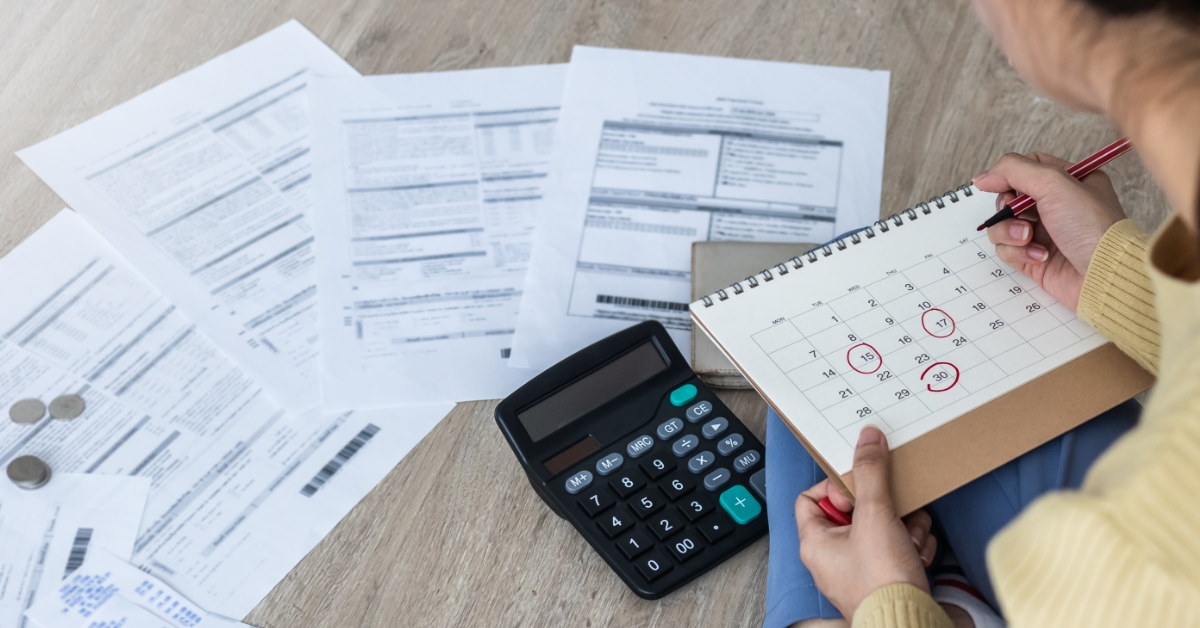 woman sitting on floor reviewing utility bills while marking calendar 