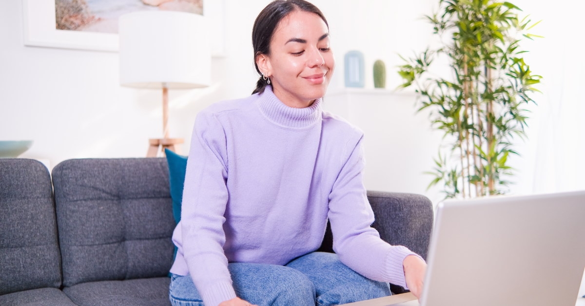 woman sitting on couch at home using calculator and laptop on table
