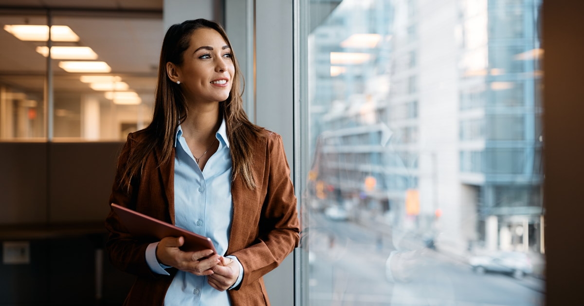 beautiful business woman holding touchpad while looking out of window 