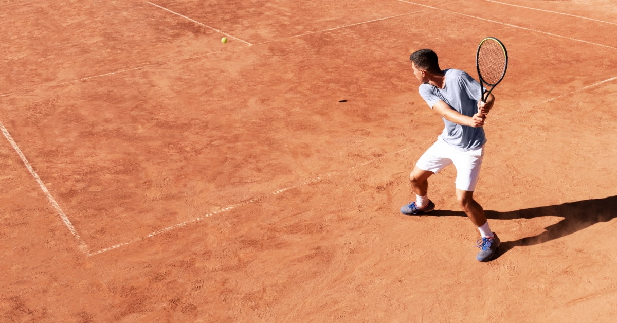 male tennis player wearing shorts playing tennis on rusty court 