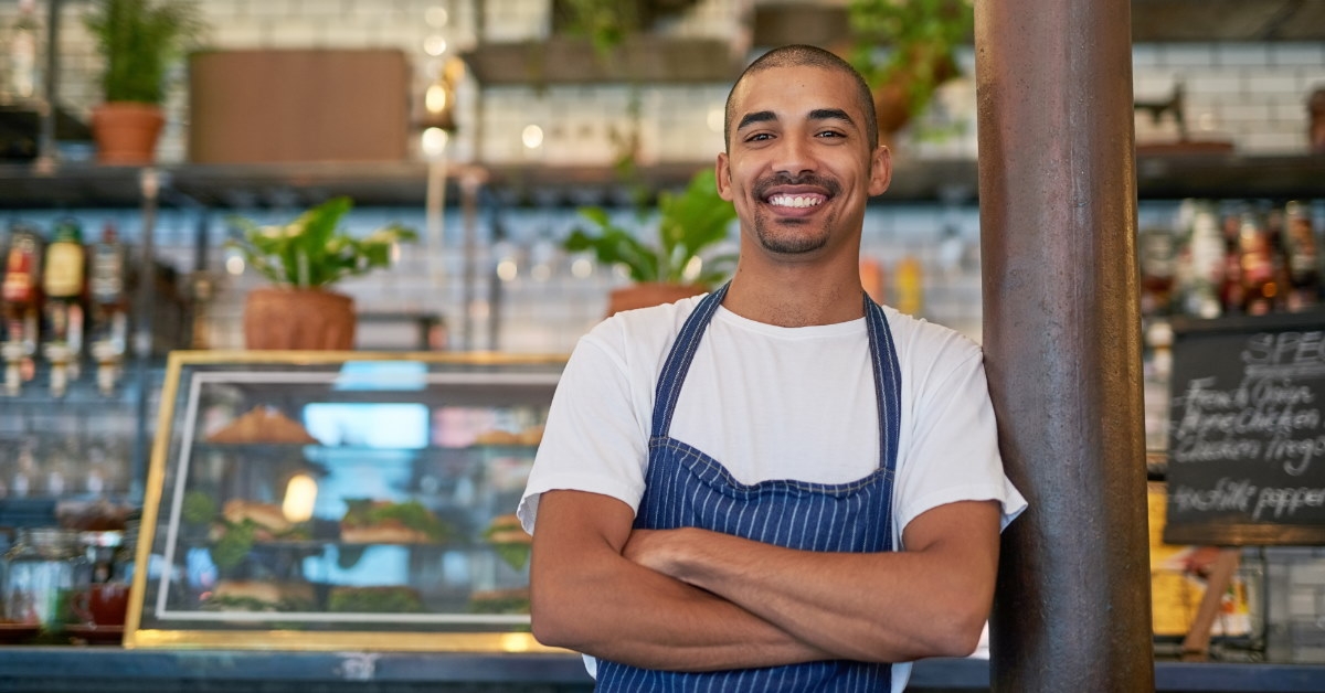 young entrepreneur smiling and posing for picture while standing inside cafe