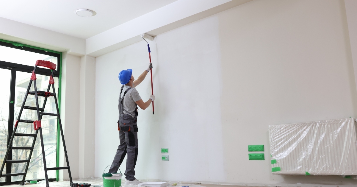 male painter paints house wall with roller brush