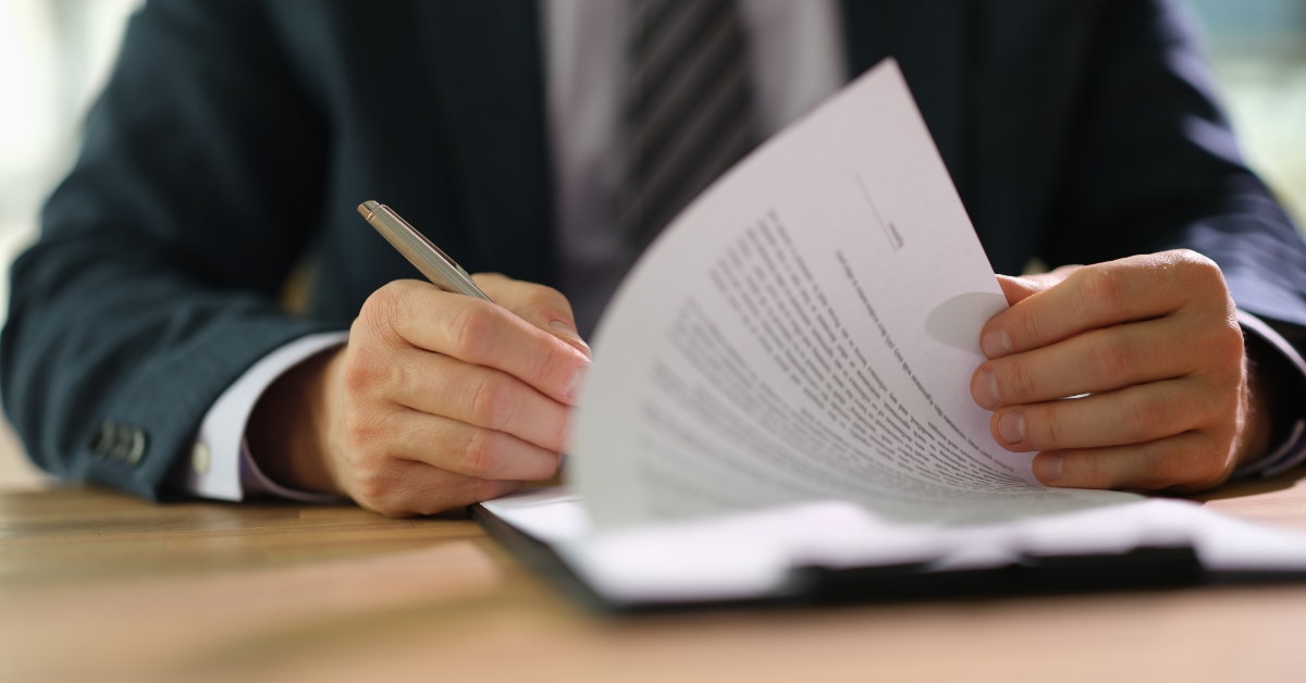 businessman wearing suit turning over pages to sign contract at table