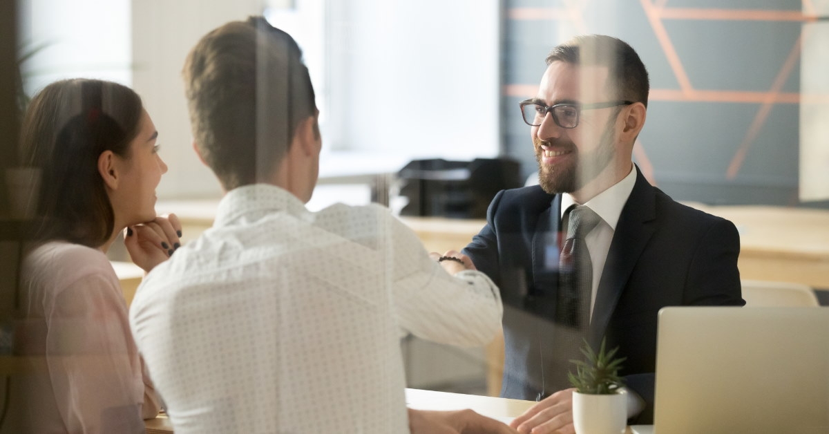 male realtor shaking hands with couple after making a deal