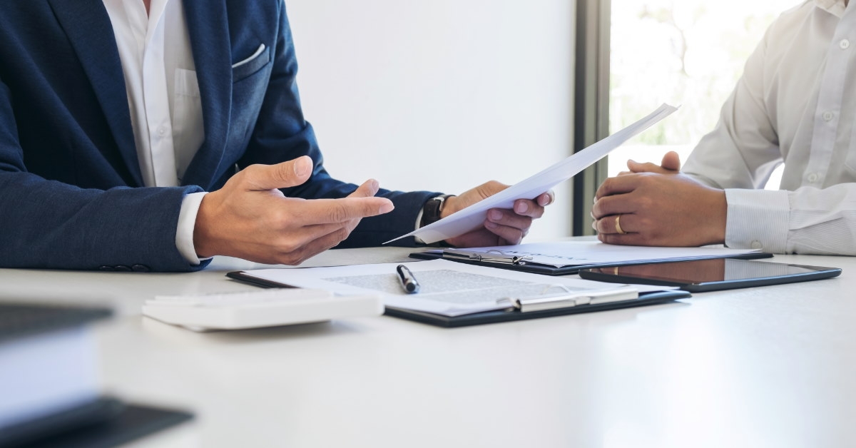 male real estate agent sitting in front of client explaining policies at table