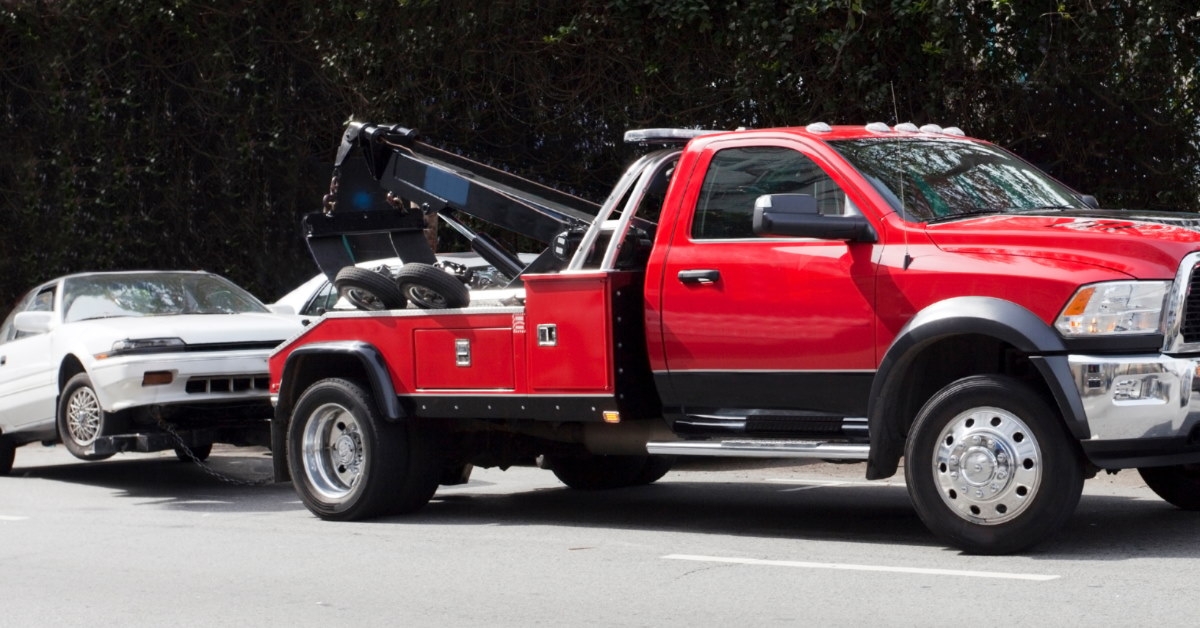 red tow truck removing white car from road on a sunny day.