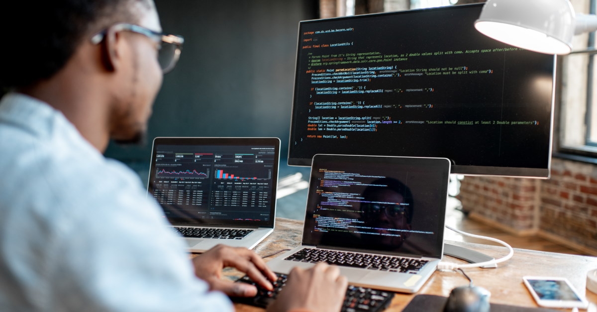 man sitting at table using laptop and desktop computer to write code
