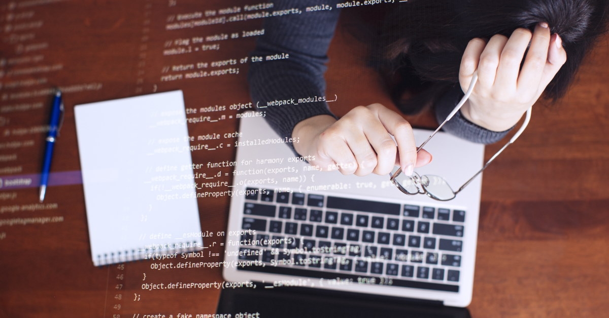 programmer coding with glasses on laptop.