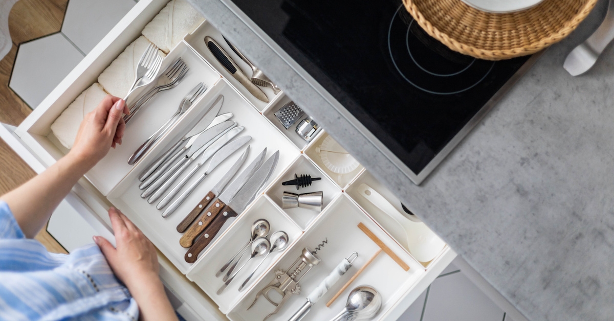 A woman grabs a fork from the utensil drawer.