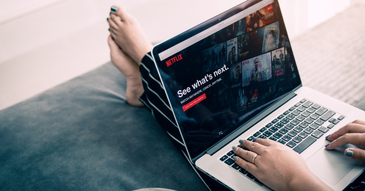 woman sitting on couch using laptop to browse netflix