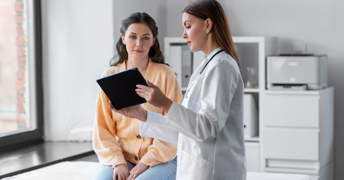 female doctor holding tablet in hand talking to female patient at clinic