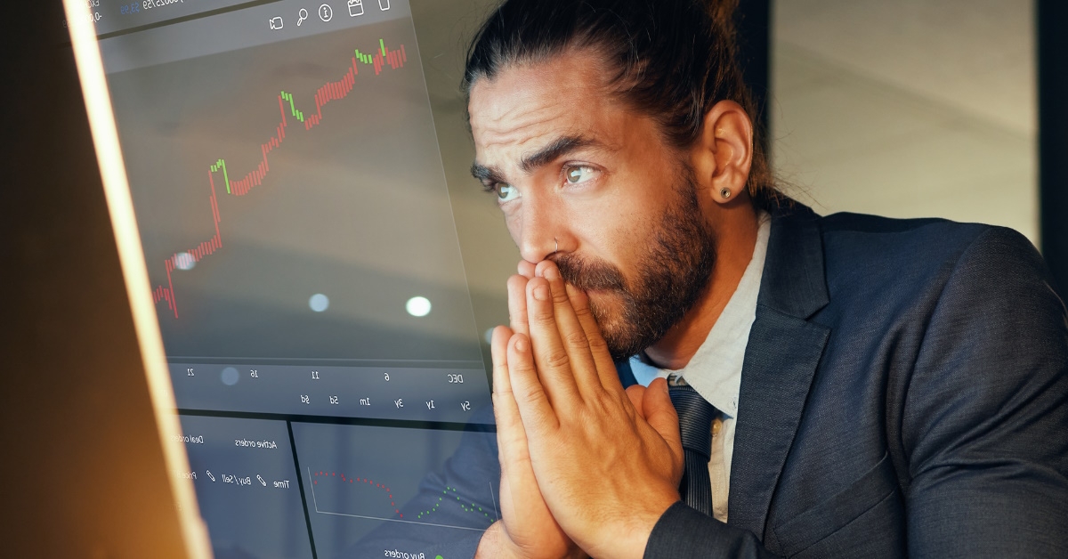 businessman holding hands in terror while stressing about stock market charts