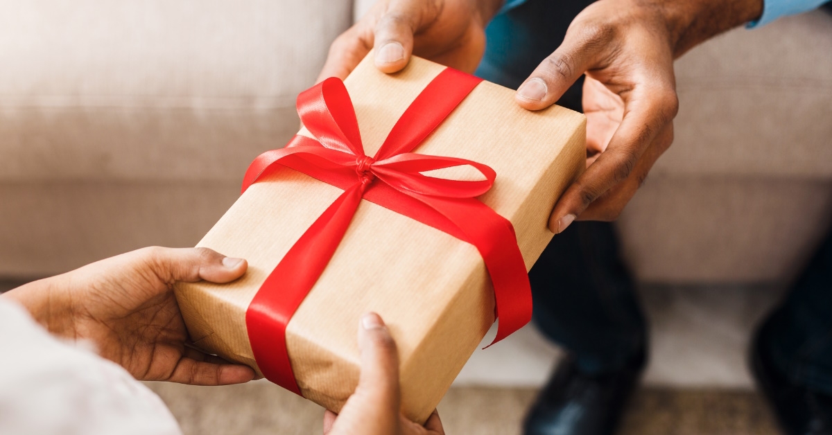 woman receiving parcel packed in brown paper and red ribbon from man