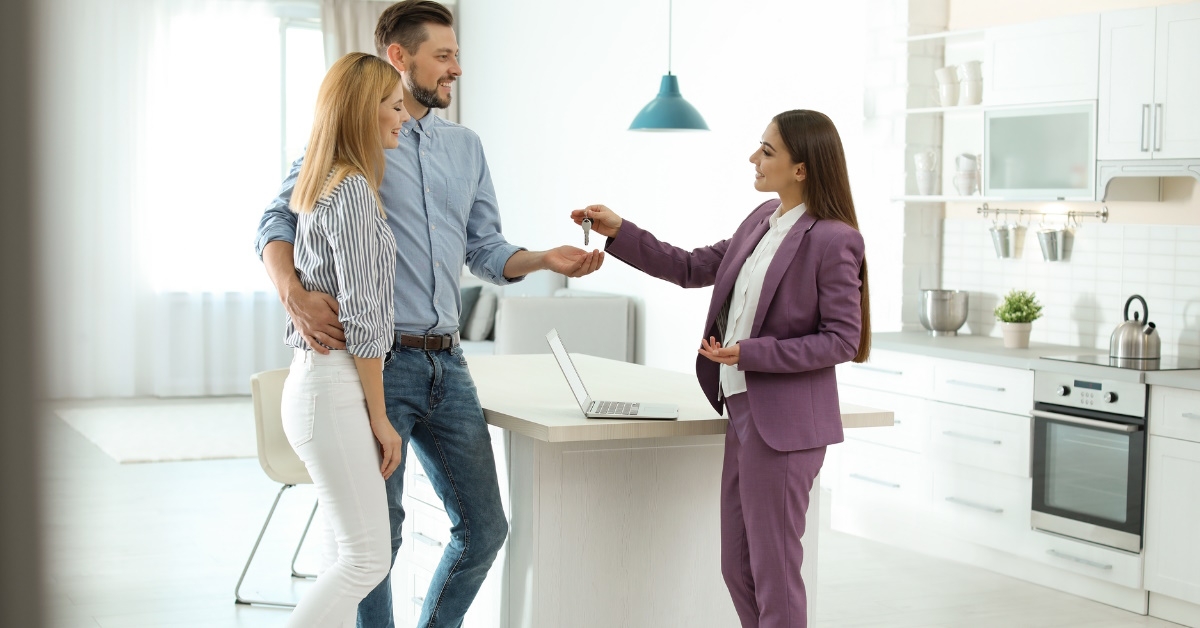 female real estate agent giving keys to young couple while standing inside new house