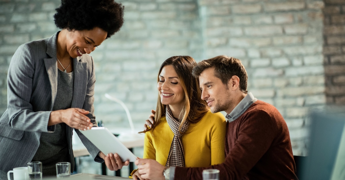 african american woman as finance advisor showing policies on tablet to young couple at office