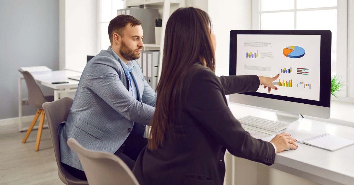 colleagues sitting at table using computer discussing business charts on display