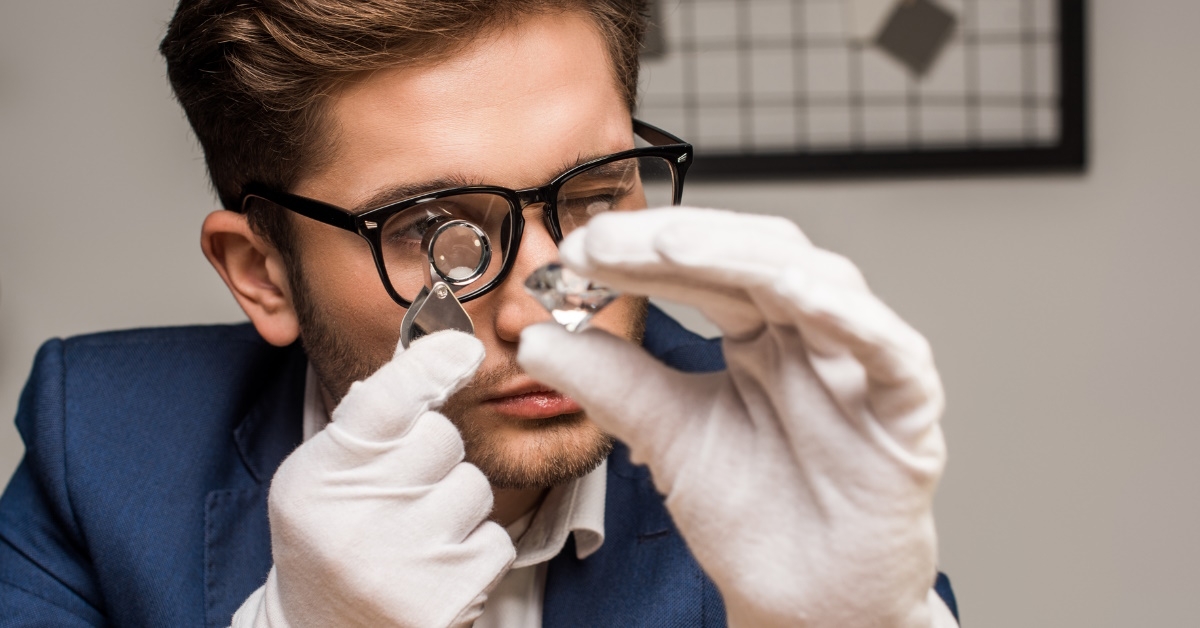 handsome male jweller in blue suit inspecting gemstone using magnifying glass at work