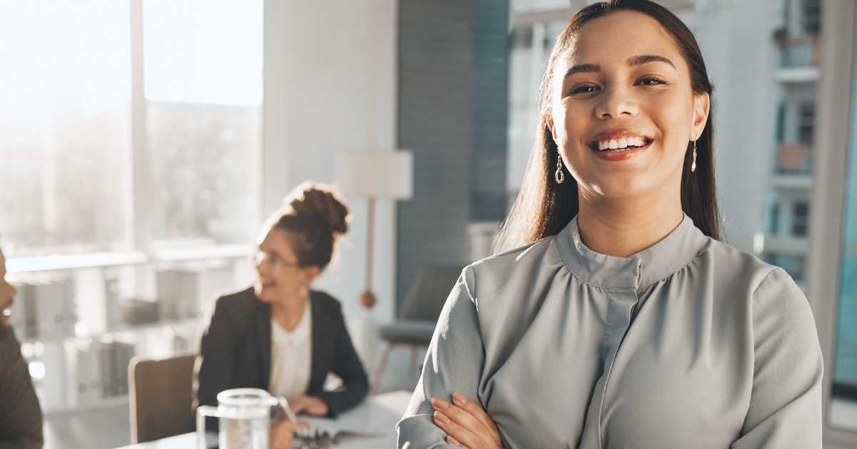 proud business woman standing in conference room while folding hands with colleagues in background