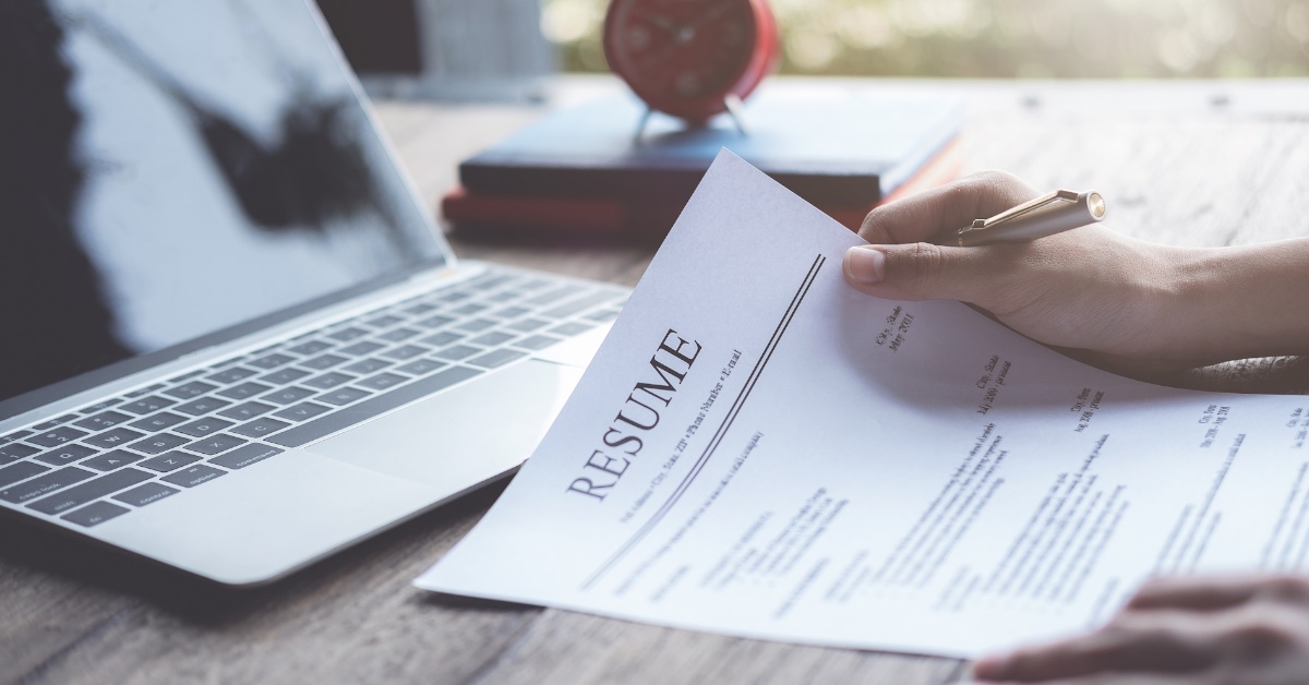 man sitting on table holding pen while reviewing resume at work