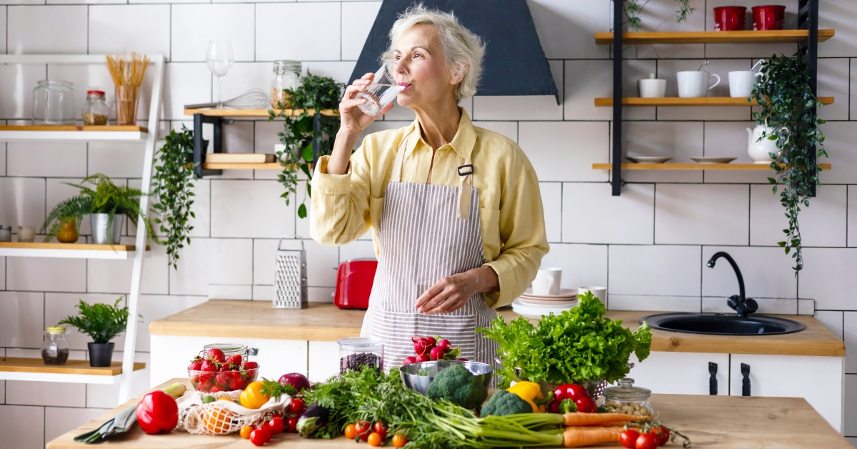 senior woman drinking water from glass while cooking