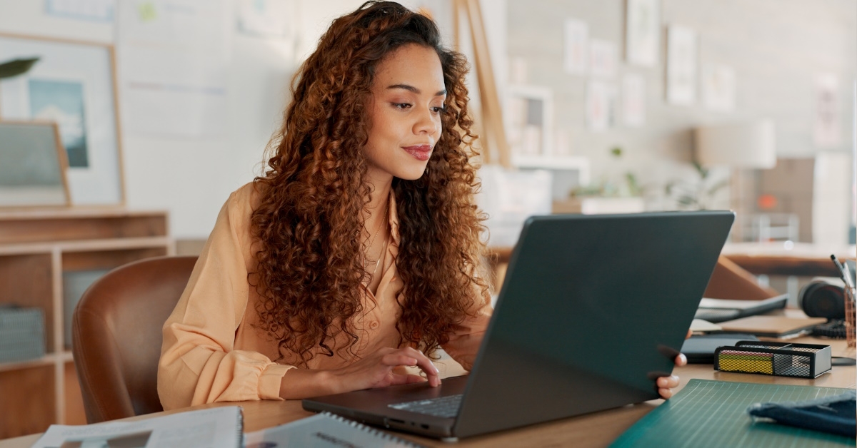 african american woman sitting at table with documents using laptop for work