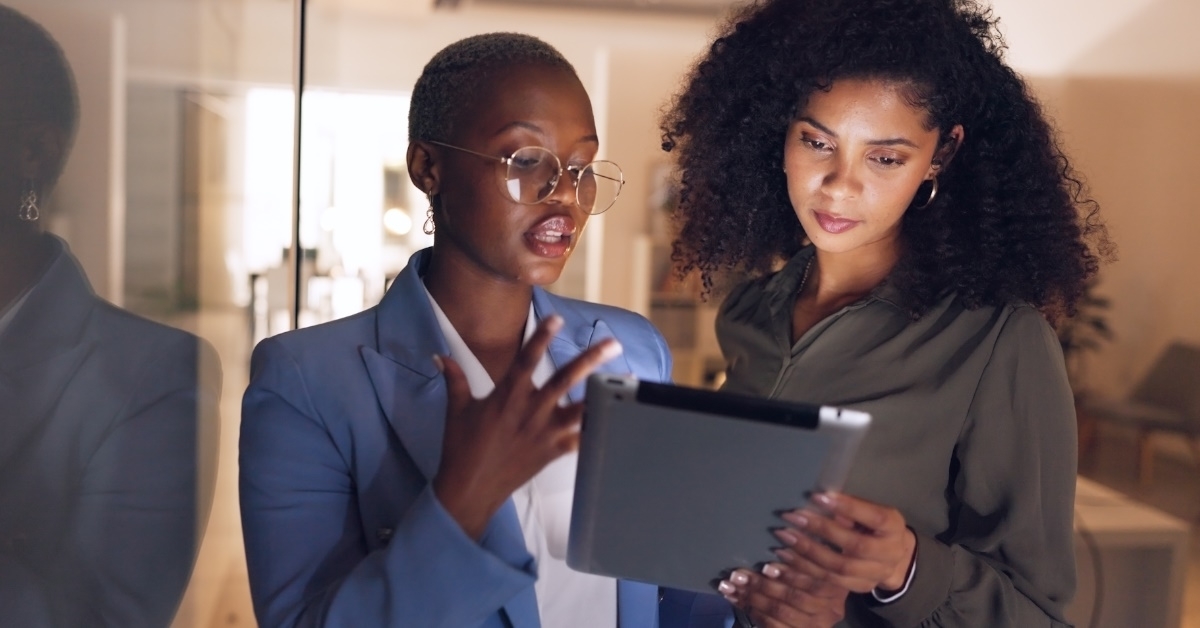 african american women standing in office discussing project together using tablet