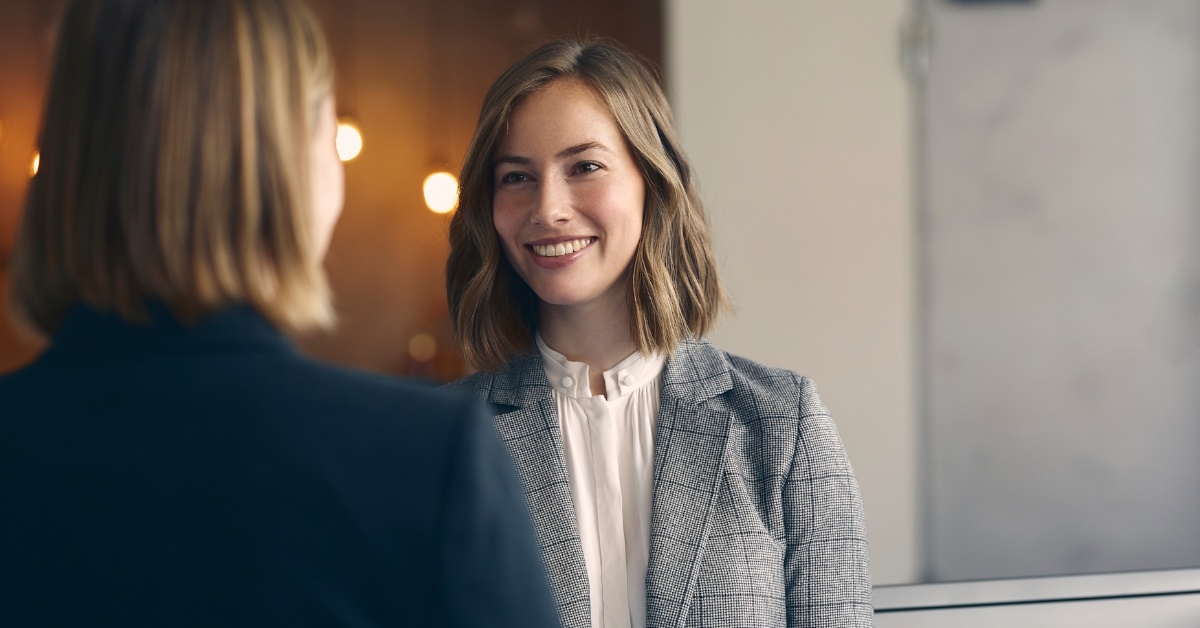 two happy female colleagues standing in front of each other in office lobby