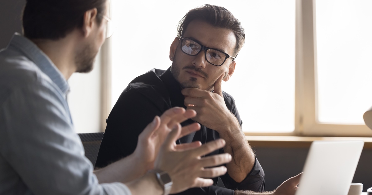 two male colleagues sitting together at one table discussing business ideas in front of laptop