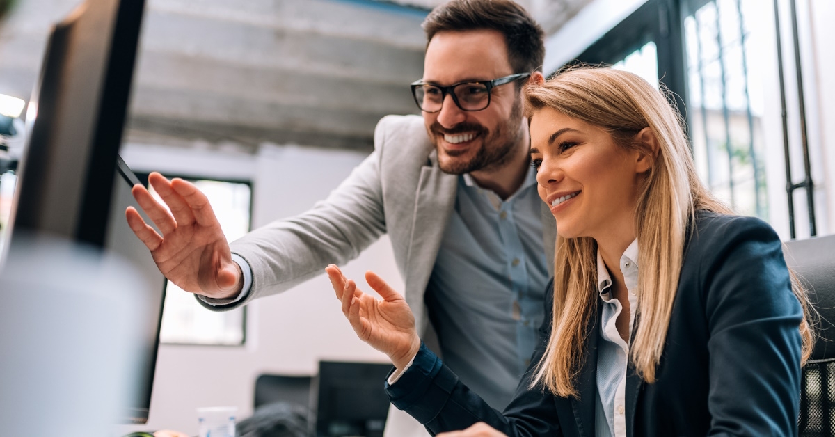 two happy colleagues using computer together to work on project at office