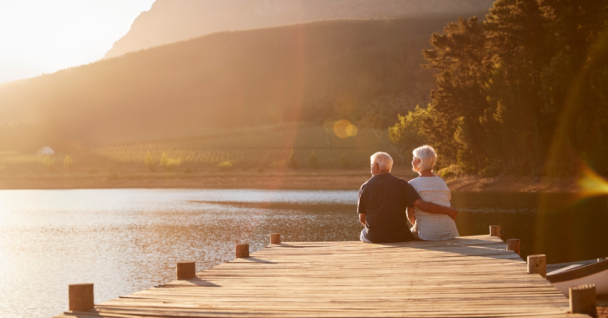 romantic senior couple sitting on wooden jetty by lake