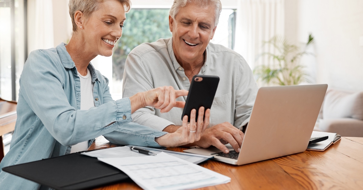 senior couple sitting at home using smartphone and laptop to plan retirement