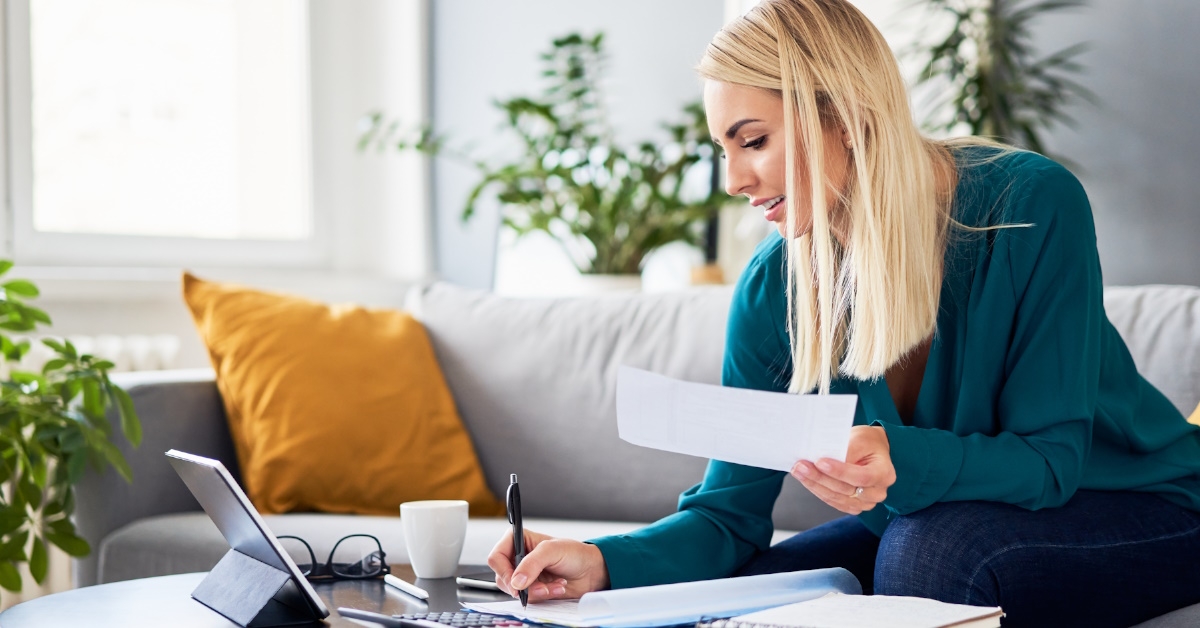 woman sitting on couch at home writing on papers to file tax