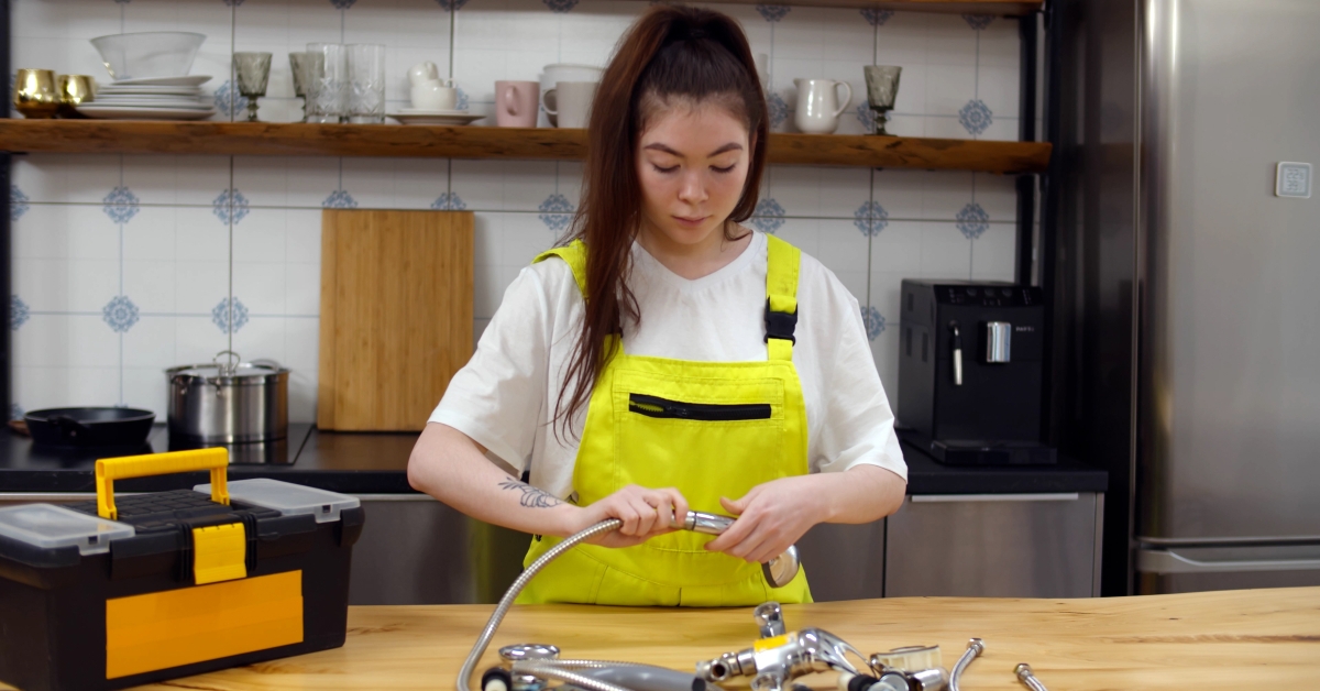 woman plumber assembling showerhead at kitchen table