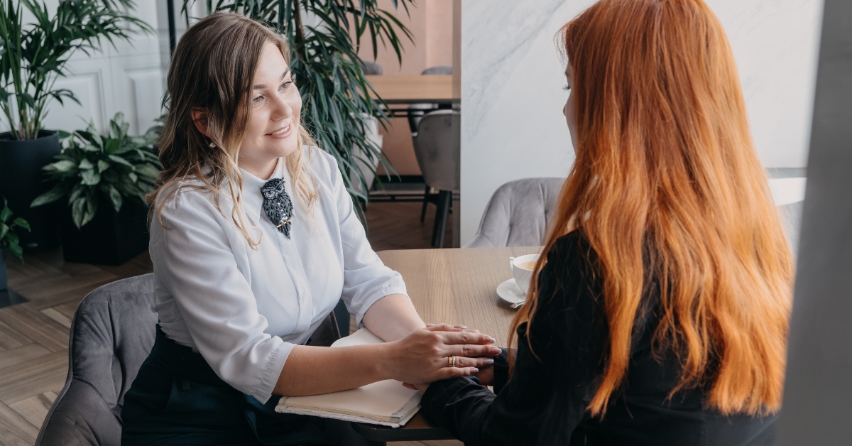 young woman comforting her friend sitting in cafe