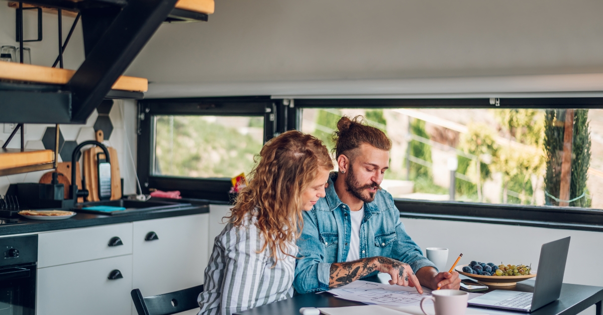 happy couple using laptop and looking into blueprints