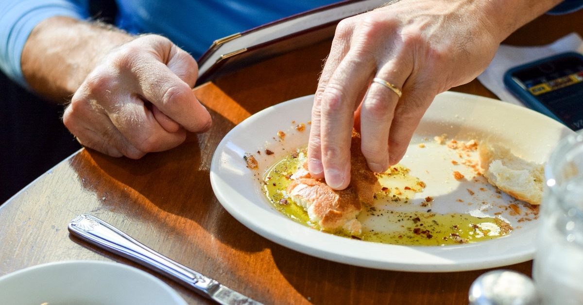 man sitting at table dipping fresh bread in plate of olive oil