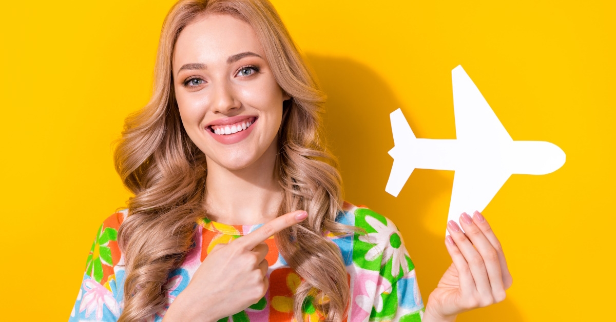 beautiful woman smiling while pointing finger towards airplane cutout over yellow background