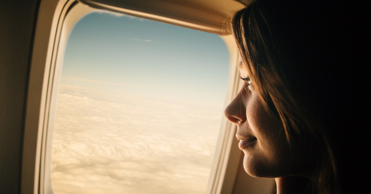 woman sitting in airplane looking out at clouds from window