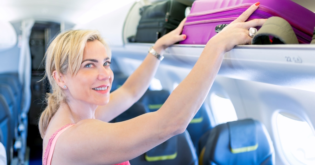 woman standing in airplane storing suitcase in airplane cabin