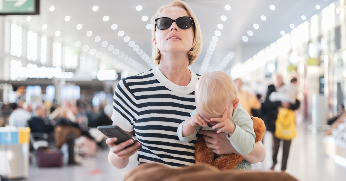 woman wearing sunglasses holding baby while waiting at desk in airport