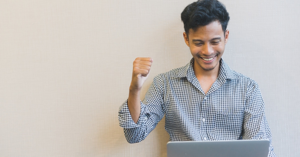 young boy sitting at floor cheering up while using laptop