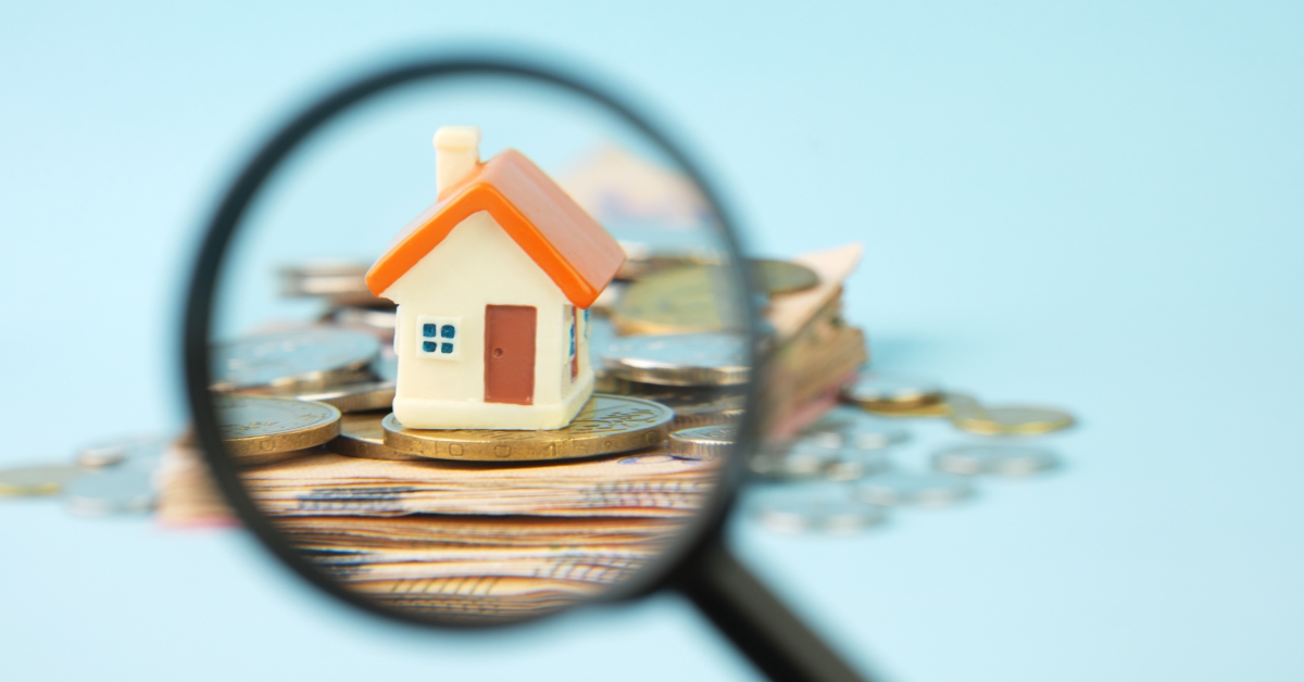 miniature house and money under a magnifying glass