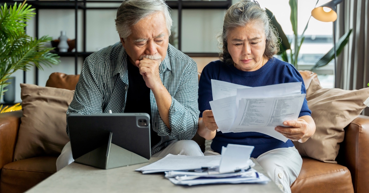senior asian couple sitting on couch with tablet on table reviewing bills at home