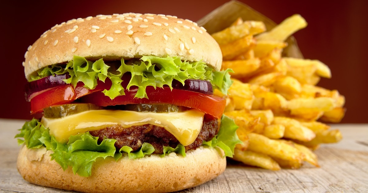 cheeseburger with melted cheese, large slices of onion and tomato withfrench fries on a wooden table 