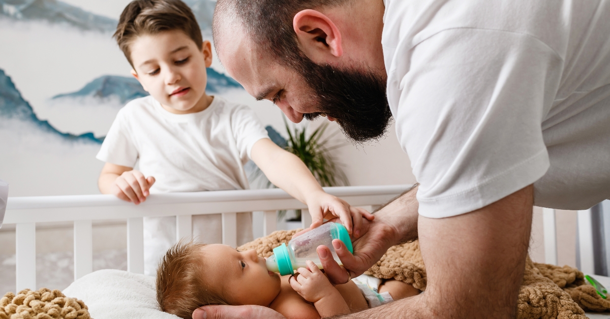 father and brother feed newborn with formula