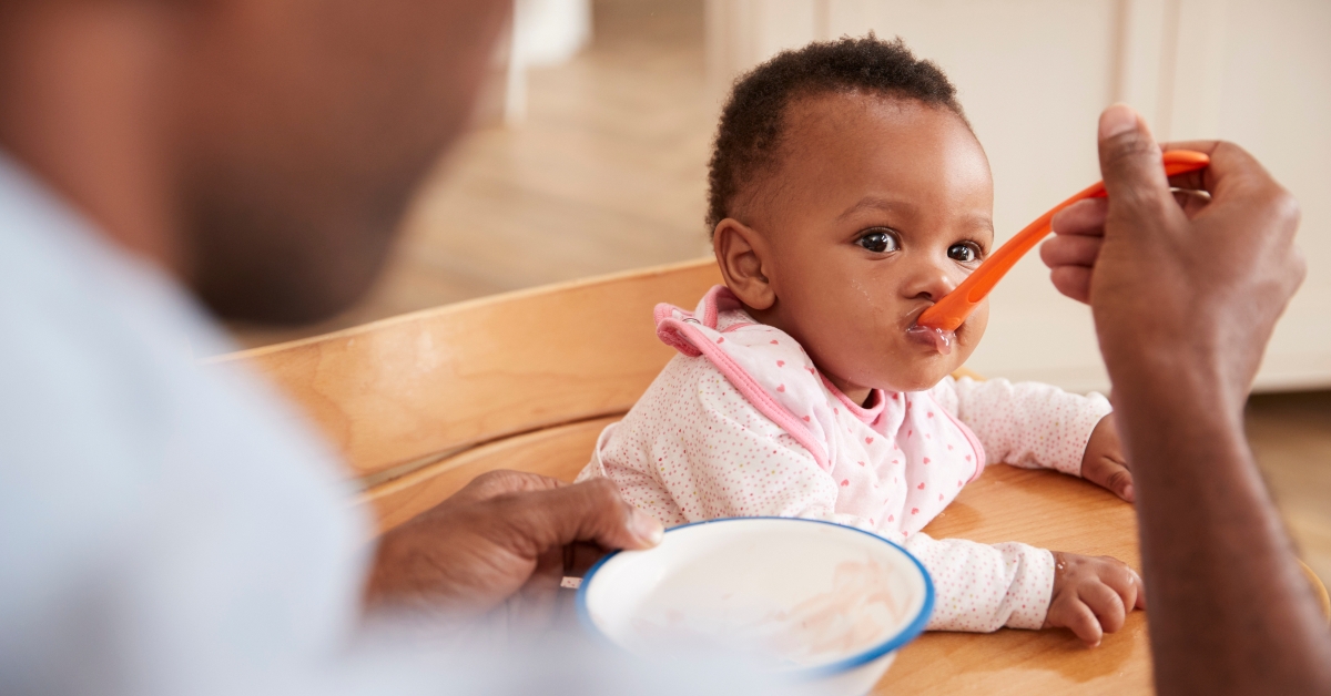 father feeding baby daughter in high chair