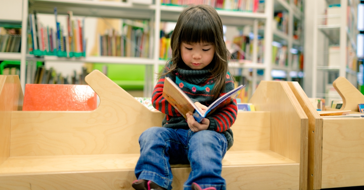 little girl reading a book in a library