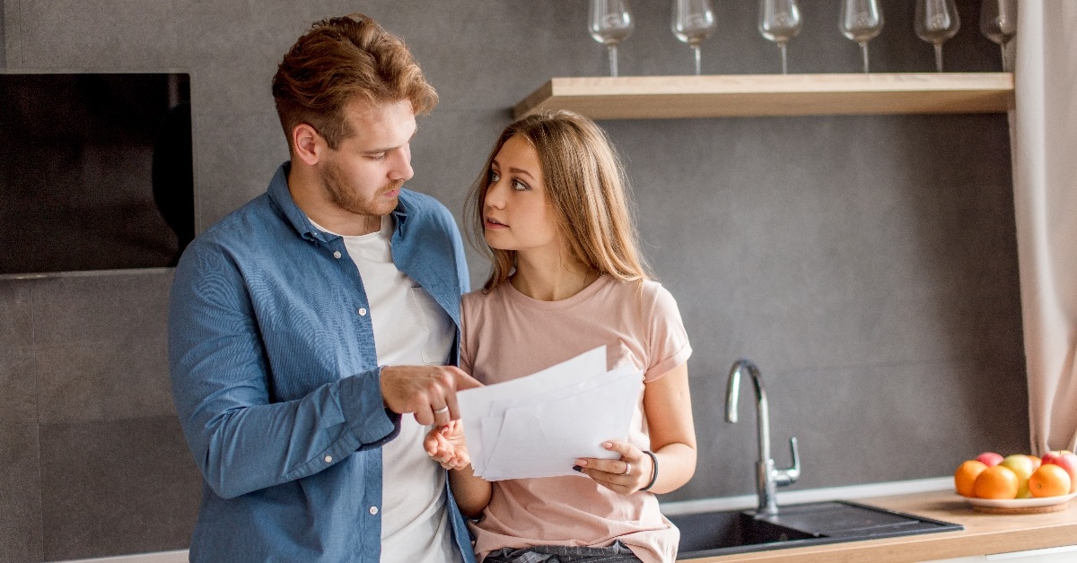 couple standing in kitchen at home reviewing bills