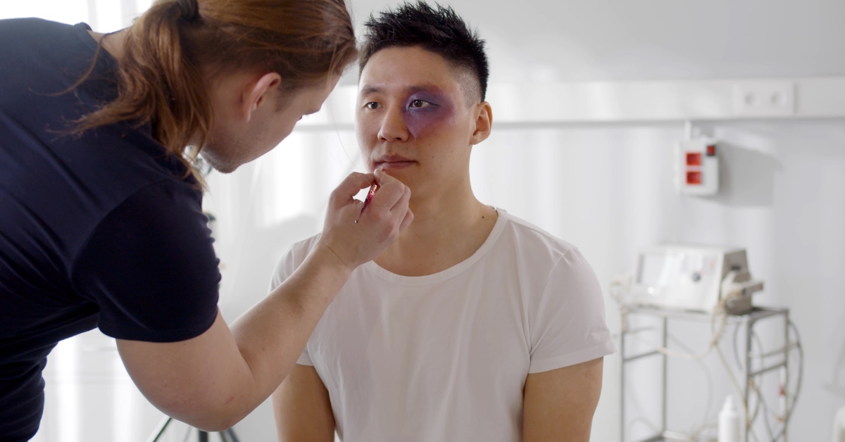 female makeup artist doing make up on actor during film shooting on movie set